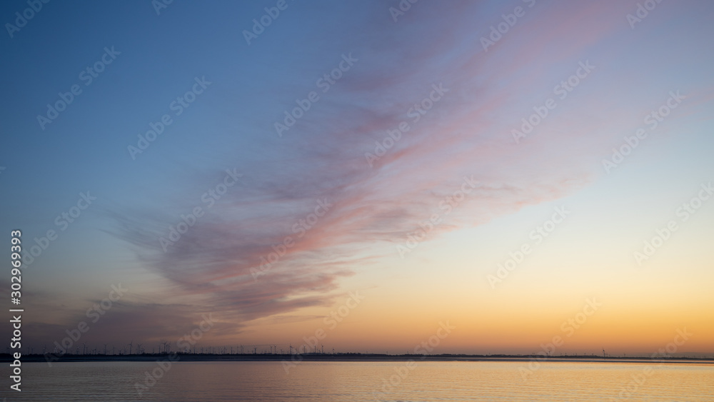 Sonnenuntergang an der Nordseeküste über einem Windenergiepark in gold und blau