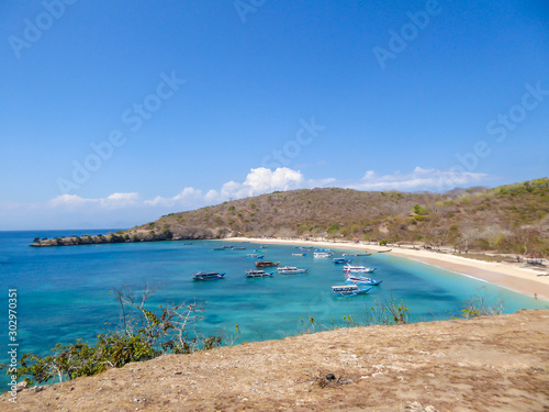 A view on a bay on Pink Beach, Lombok Indonesia. Plenty colourful boats anchored to the shore. The water has many shades of blue. The heavenly beach is surrounded by small hills. Paradise beach. © Chris