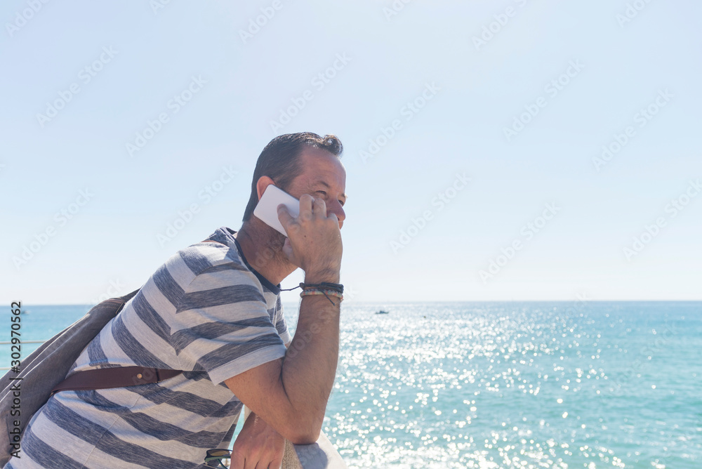 Young man in t-shirt standing on seashore while using a mobile phone