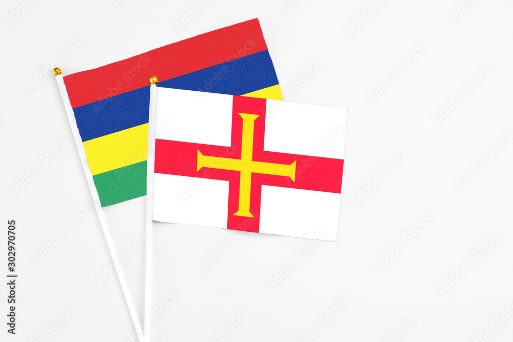 Guernsey and Mauritius stick flags on white background. High quality fabric, miniature national flag. Peaceful global concept.White floor for copy space.