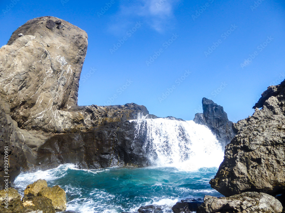 Wave waterfall on Pantai Nambung, Lombok, Indonesia.The water crushes on the rocks on shore, breaching through them, creating a temporary waterfall. The rock formation looks very sharp and dangerous