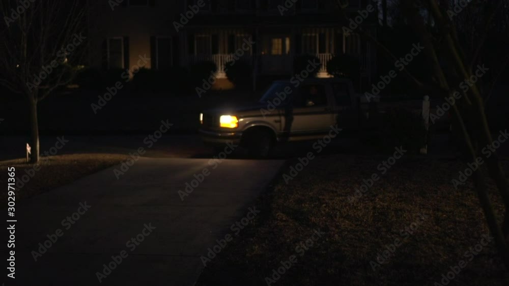 An old truck pulling up in a driveway at night.