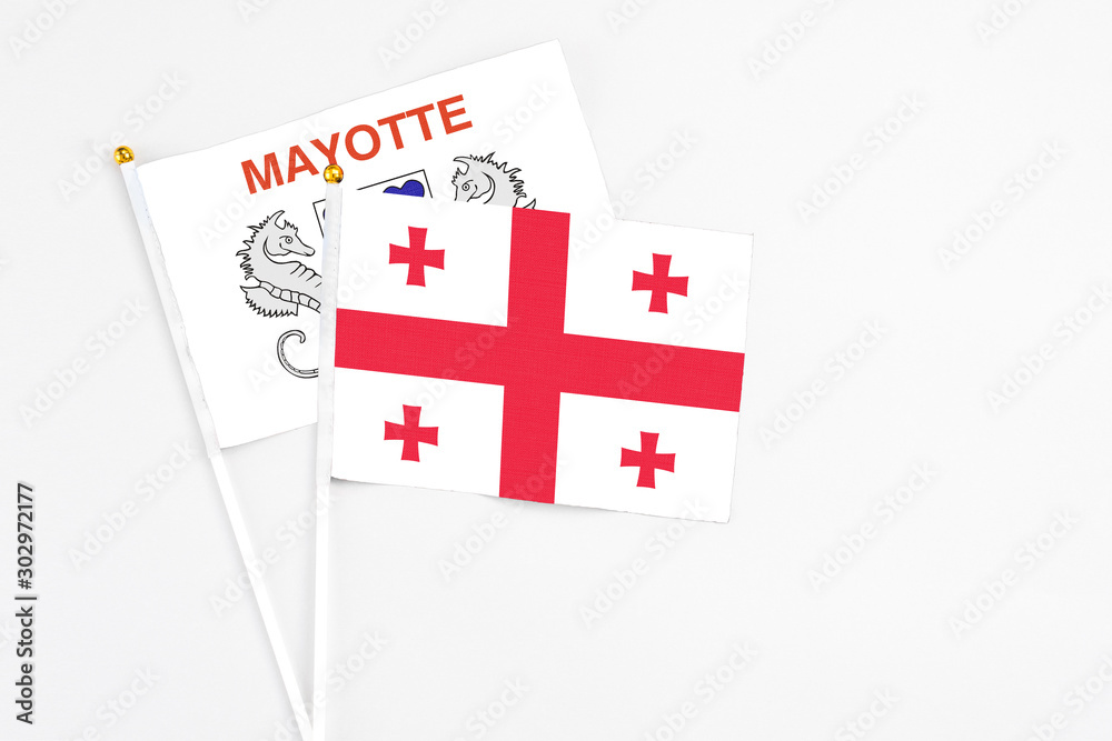 Georgia and Mayotte stick flags on white background. High quality fabric, miniature national flag. Peaceful global concept.White floor for copy space.