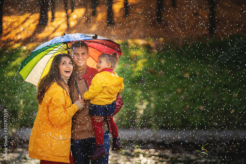 Happy funny family with colourful umbrella under the autumn rain.