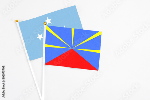 Reunion and Micronesia stick flags on white background. High quality fabric, miniature national flag. Peaceful global concept.White floor for copy space.