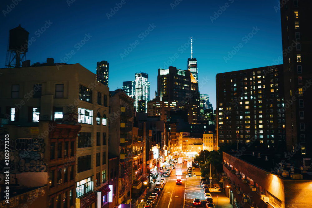 Evening cityscape of tall building shining with lights from windows and traffic on roads, urban setting in downtown district with modern architecture with real estate for residence or business.