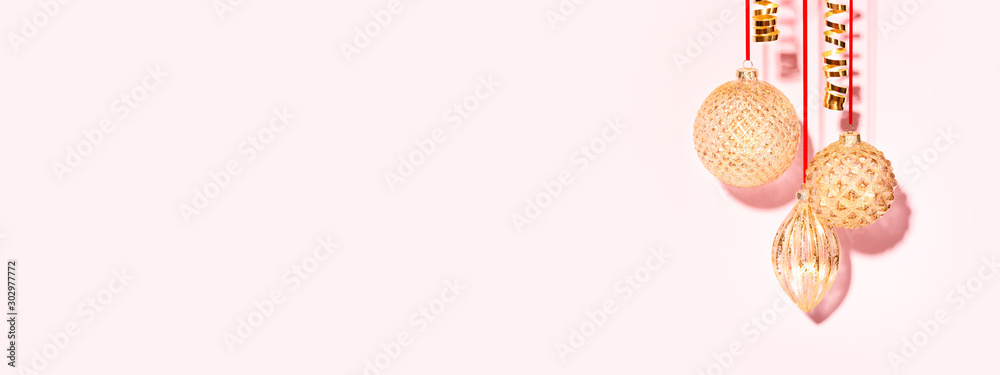 Banner with three golden Christmas baubles hanging against the pink background. Minimal styled New Year concept. Banner with three golden Christmas baubles hanging against the pink background. Minimal styled New Year concept.