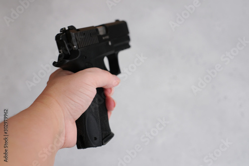 Woman holding gun in her hand at home. Focus hand of young women using black gun on gray background.