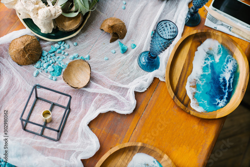 Marine decor on a festive wooden table. Plate with epoxy resin in the form of sea waves, coconut and blue glasses