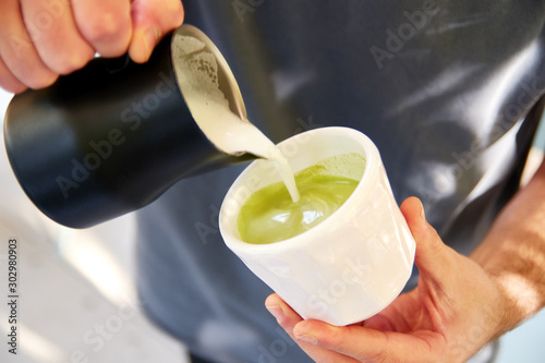 Male barista making vegan matcha cappuccino with oat milk