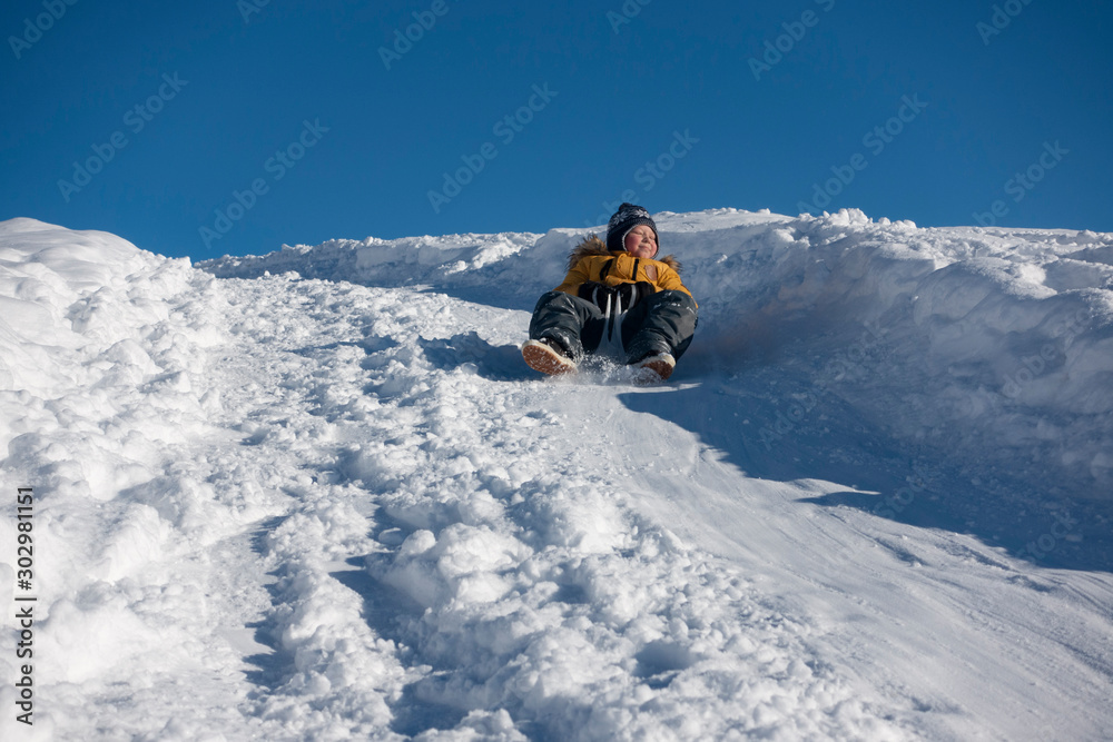 happy boy sliding down snow hill on sled outdoors in winter, sledging and  season concept Stock Photo