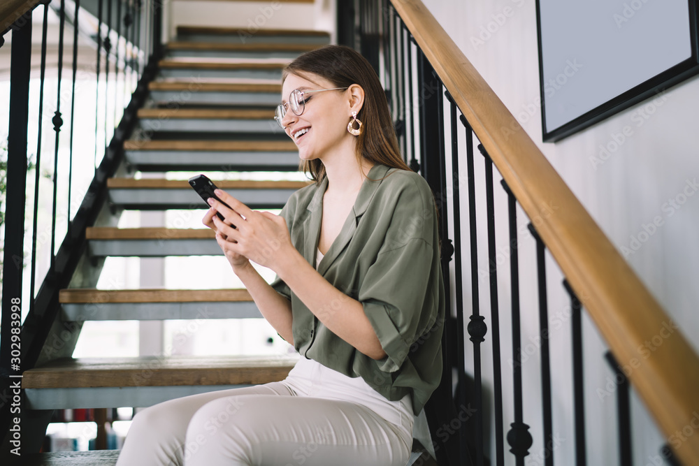 Fototapeta premium Satisfied female resting on stairs and messaging on cellphone