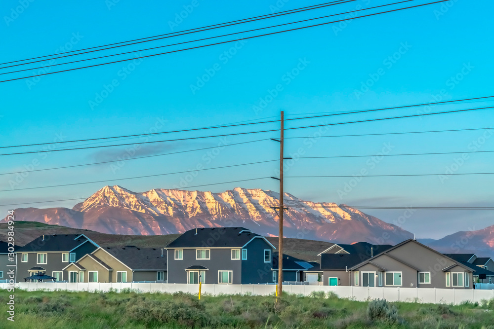 Neighborhood homes with sunlit snow capped mountain and blue sky background