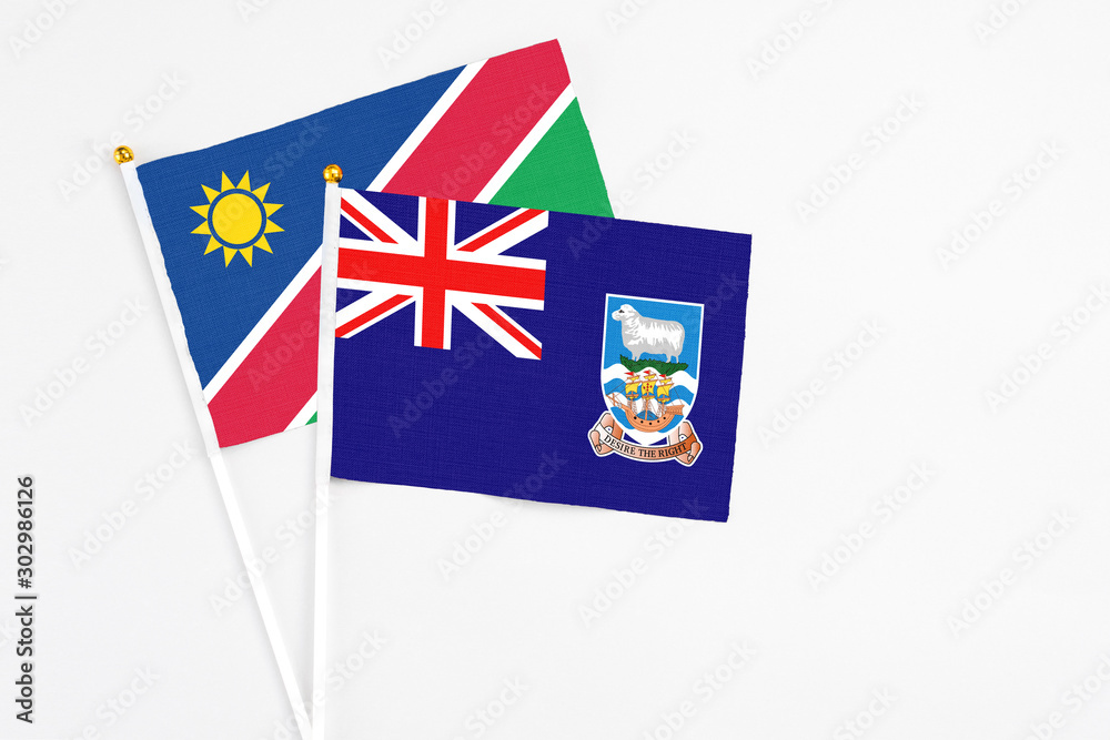Fototapeta premium Falkland Islands and Namibia stick flags on white background. High quality fabric, miniature national flag. Peaceful global concept.White floor for copy space.