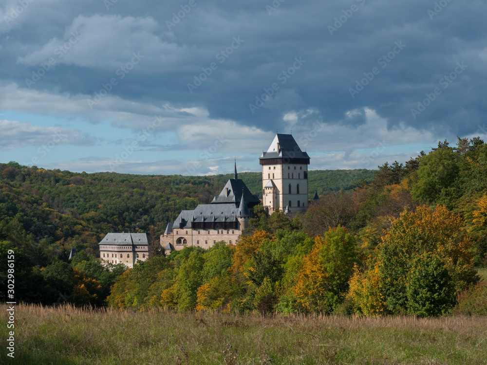 Karlstejn gothic state castle near Prague, the most famous castle in Czech Republic with grass meadow and autumn colored trees and forest. Blue sky clouds background. Located near Prague.