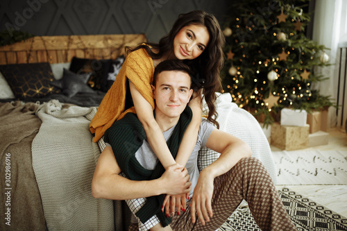 happy couple in love in the morning on the bed near the Christmas tree, hug, Christmas morning. home clothes and sweaters. comfort and warmth of hearts