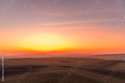 The sun caught during the last moment before setting beyond the horizon with view of a field covered with fog and the farms and fields undulating in the region of South Moravia is also called Tuscany © Lukas