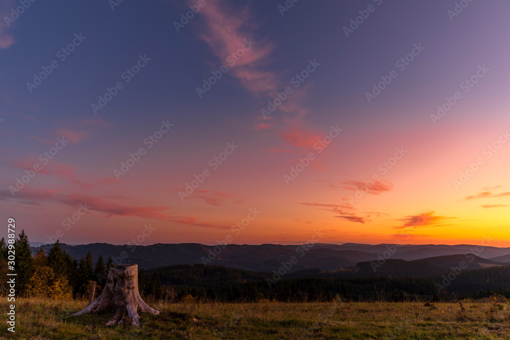 Colorful time-lapse sunset with old abandoned tree trunk and main subject colorful sky with orange and blue colors sunset captured in high mountains Beskydy area Czech Republic.
