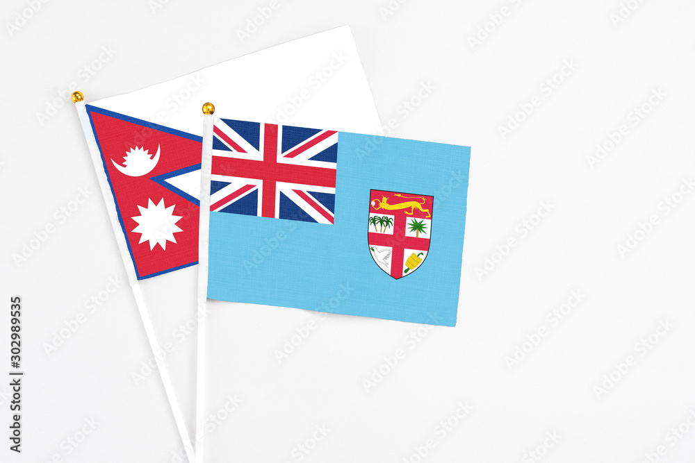 Fototapeta premium Fiji and Nepal stick flags on white background. High quality fabric, miniature national flag. Peaceful global concept.White floor for copy space.