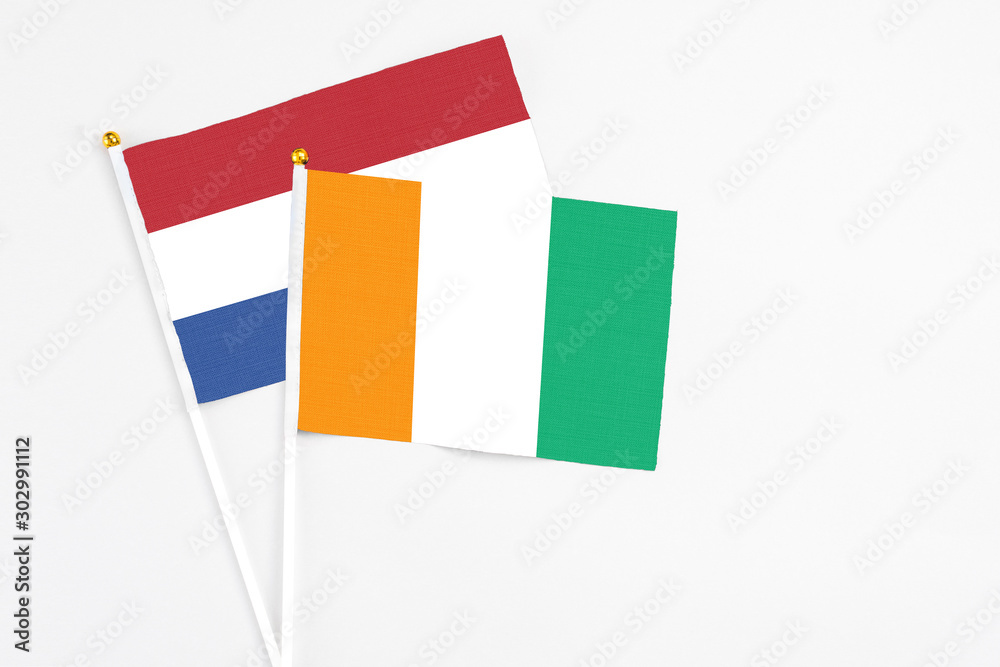 Cote D'Ivoire and Netherlands stick flags on white background. High quality fabric, miniature national flag. Peaceful global concept.White floor for copy space. Cote D'Ivoire and Netherlands stick flags on white background. High quality fabric, miniature national flag. Peaceful global concept.White floor for copy space.
