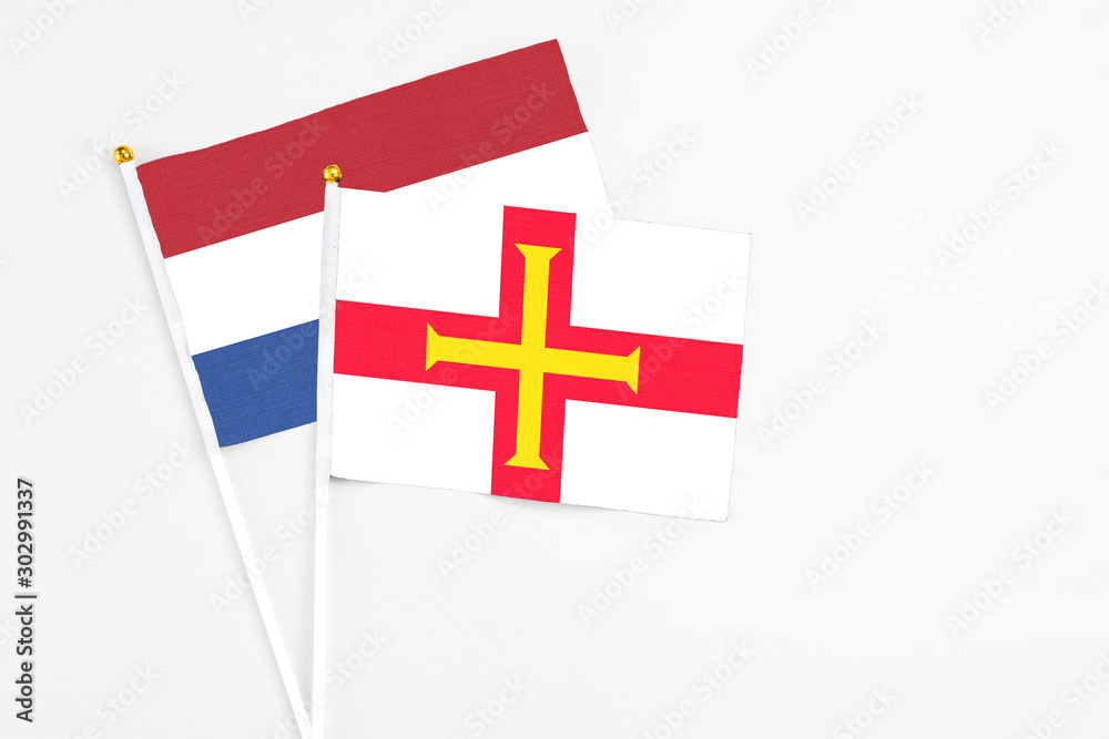 Guernsey and Netherlands stick flags on white background. High quality fabric, miniature national flag. Peaceful global concept.White floor for copy space.