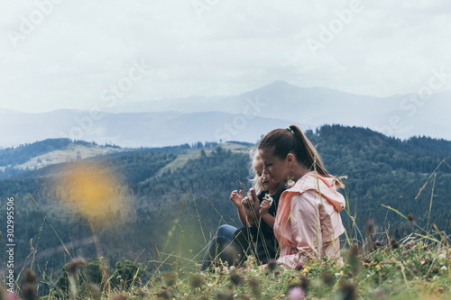 Mother and daughter sitting on hill with mountain view behind