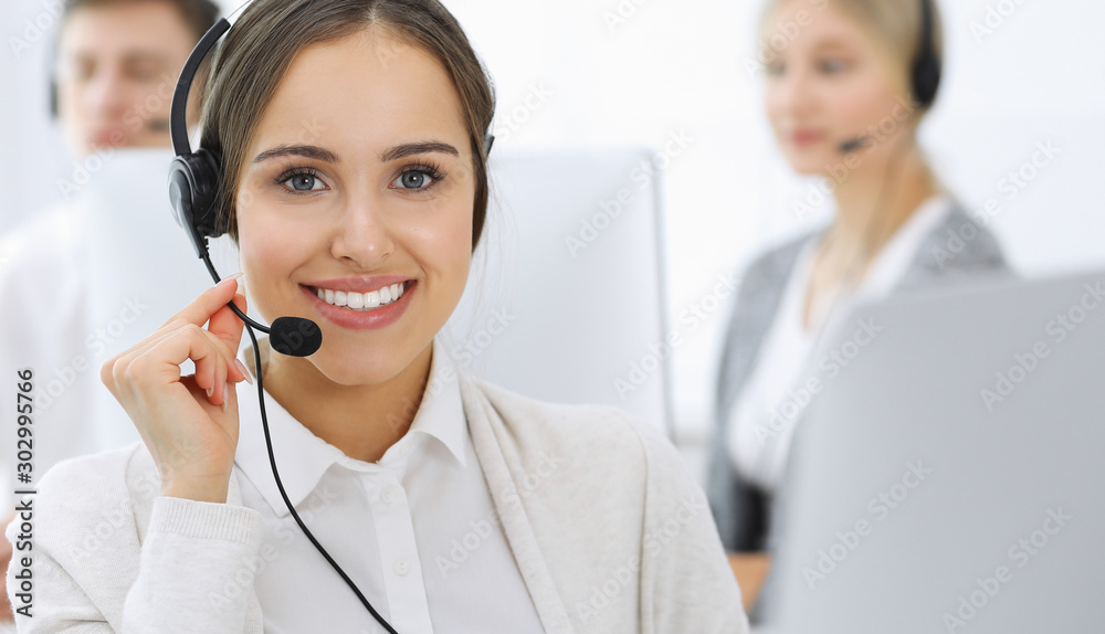 Call center. Group of operators at work. Focus on beautiful woman receptionist in headset at customer service white colored office. Business concept Call center. Group of operators at work. Focus on beautiful woman receptionist in headset at customer service white colored office. Business concept