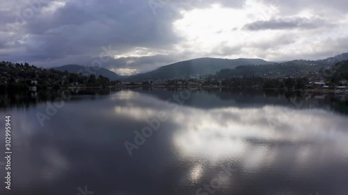 Low angle aerial shot over the calm water surface of a lake on a partly cloudy morning. photo