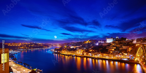 Porto, Portugal. Evening sunset panoramic view at nighttime town and Ponte de Dom Luis bridge with tramways. Coastline of river Douro with reflections of illumination in water and picturesque clouds.