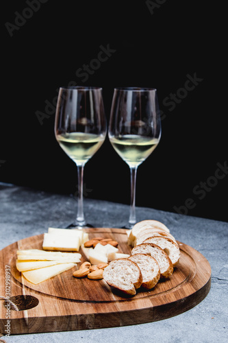Cheese, nuts and tiny bread for brunch on a wooden plate ad white wine