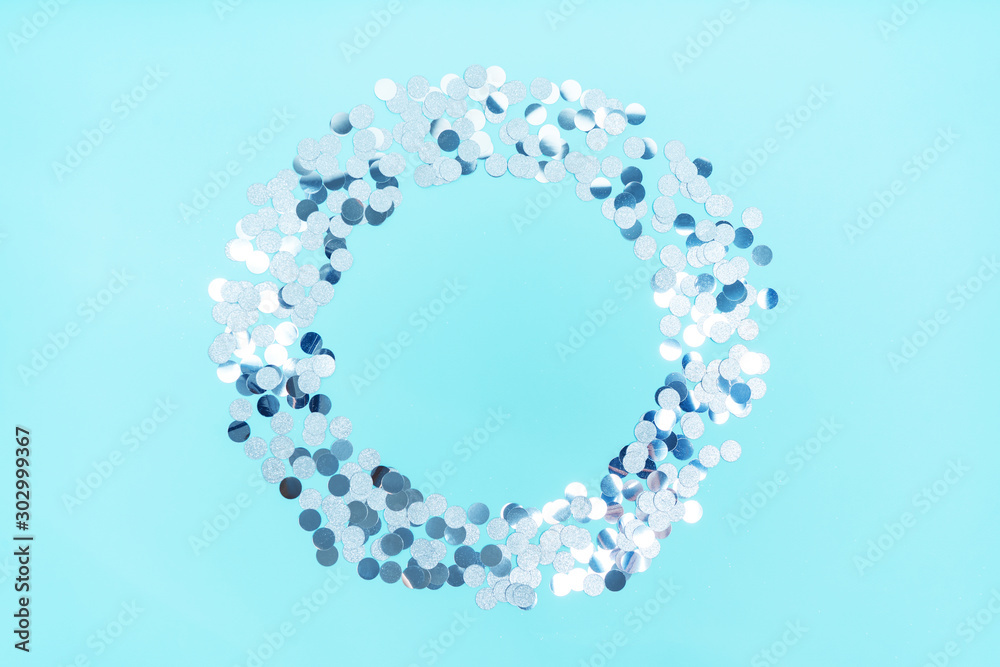 Silver shiny confetti in the form of a round frame on a blue background with a copy of the space. Silver shiny confetti in the form of a round frame on a blue background with a copy of the space.