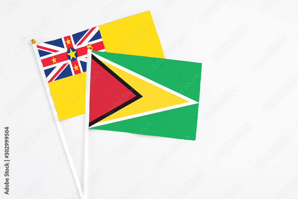 Guyana and Niue stick flags on white background. High quality fabric, miniature national flag. Peaceful global concept.White floor for copy space.
