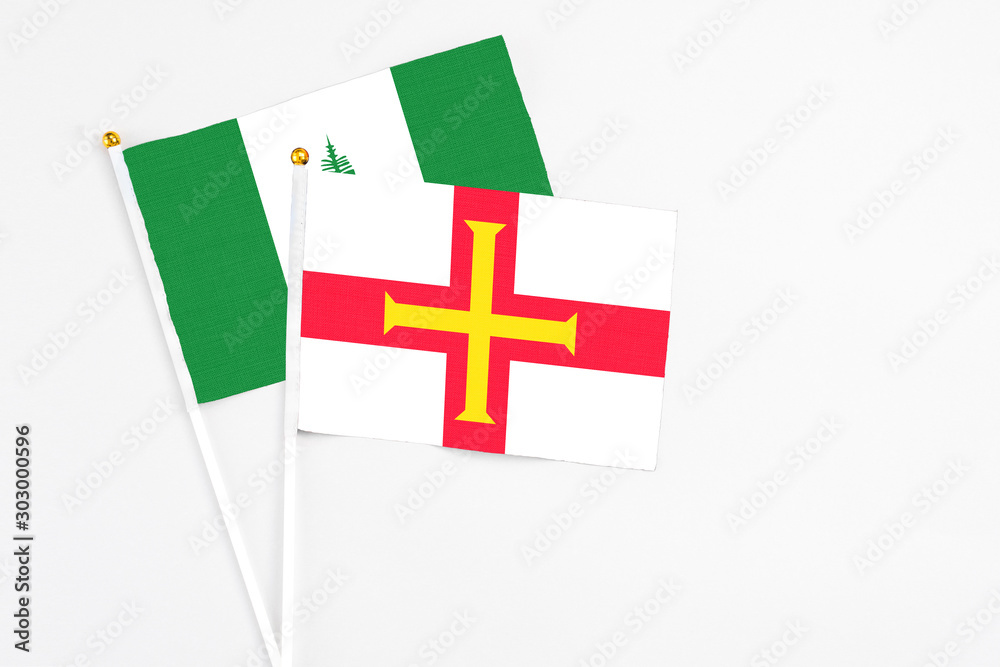 Guernsey and Norfolk Island stick flags on white background. High quality fabric, miniature national flag. Peaceful global concept.White floor for copy space.