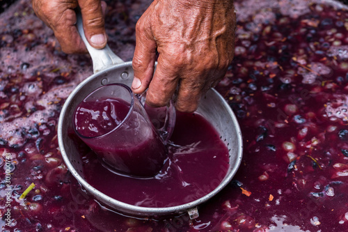 Winemaker's hand with a glass mug, picking up juice from grape must. Wine material, stum, maun. Technology of wine production in Moldova. The folk tradition of making wine.