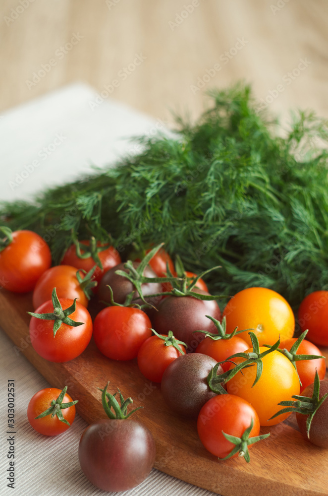 Beautiful tomatoes and dill lie on a cutting board and on a light tablecloth. Beautiful tomatoes and dill lie on a cutting board and on a light tablecloth.