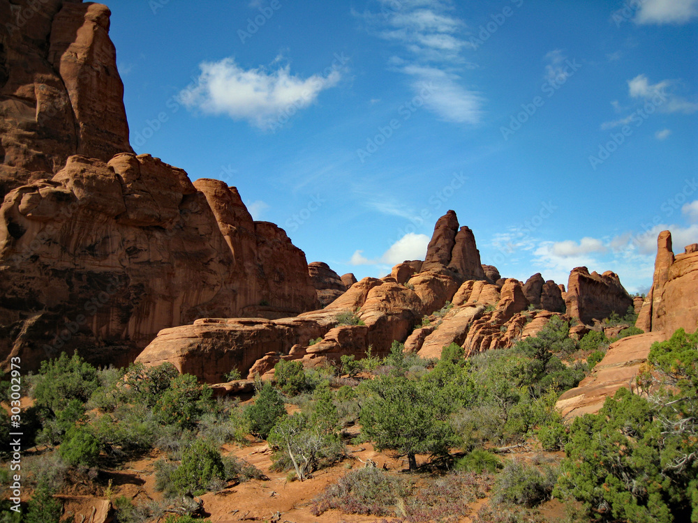 Vertical rust-red sandstone fins of Arches National Park in Utah, USA, contrast well against the bright blue sky and green scrubby vegetation