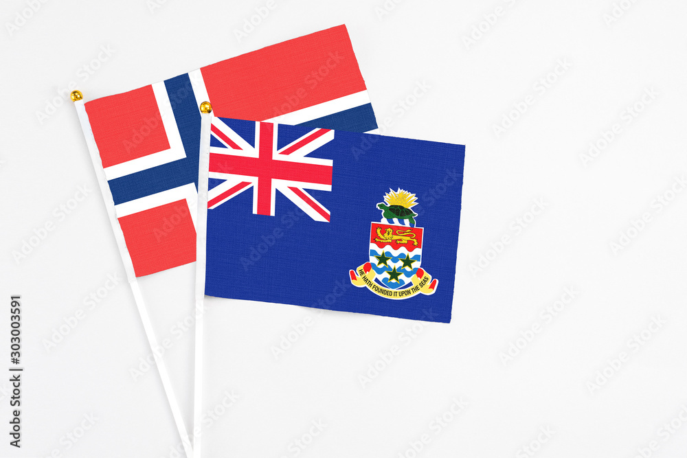 Fototapeta premium Cayman Islands and Norway stick flags on white background. High quality fabric, miniature national flag. Peaceful global concept.White floor for copy space.