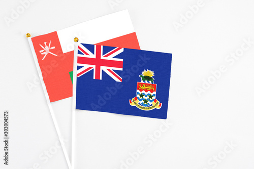 Cayman Islands and Oman stick flags on white background. High quality fabric, miniature national flag. Peaceful global concept.White floor for copy space.
