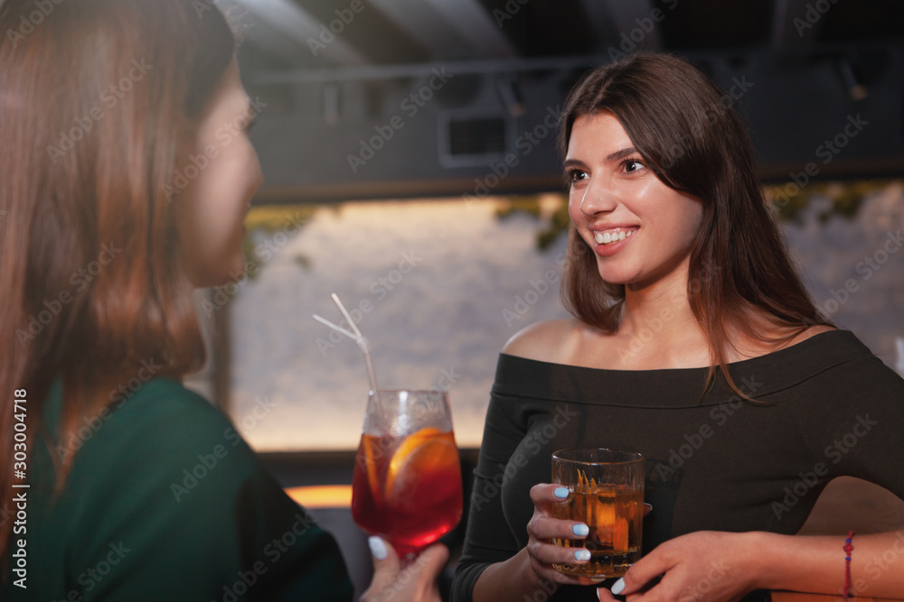 Attractive cheerful woman enjoying drinks with her friend at the restaurant in the evening Attractive cheerful woman enjoying drinks with her friend at the restaurant in the evening