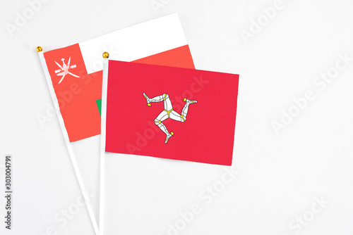 Isle Of Man and Oman stick flags on white background. High quality fabric, miniature national flag. Peaceful global concept.White floor for copy space.
