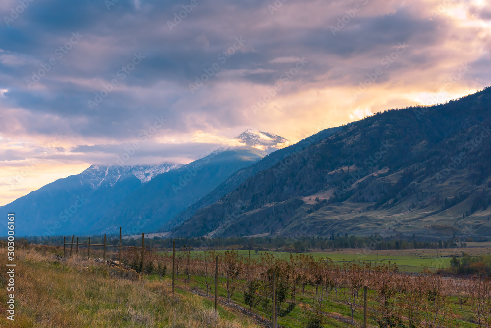 View from Crowsnest highway of autumn valley with view of snow-capped mountain and dramatic clouds at sunset in Cawston, BC, Canada