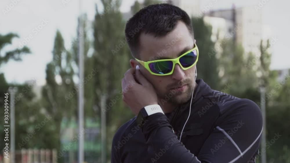 Theme sport and health. A young Caucasian man uses a smartphone smarfton to listen to music on headphones. Technology and mobile application playlist on the city stadium track treadmill