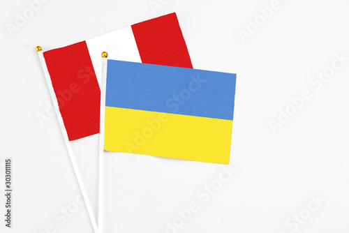 Ukraine and Peru stick flags on white background. High quality fabric  miniature national flag. Peaceful global concept.White floor for copy space.