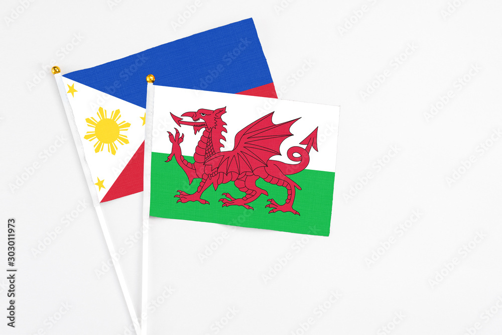 Obraz premium Wales and Philippines stick flags on white background. High quality fabric, miniature national flag. Peaceful global concept.White floor for copy space.