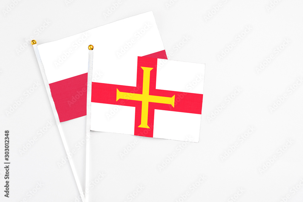 Guernsey and Poland stick flags on white background. High quality fabric, miniature national flag. Peaceful global concept.White floor for copy space.