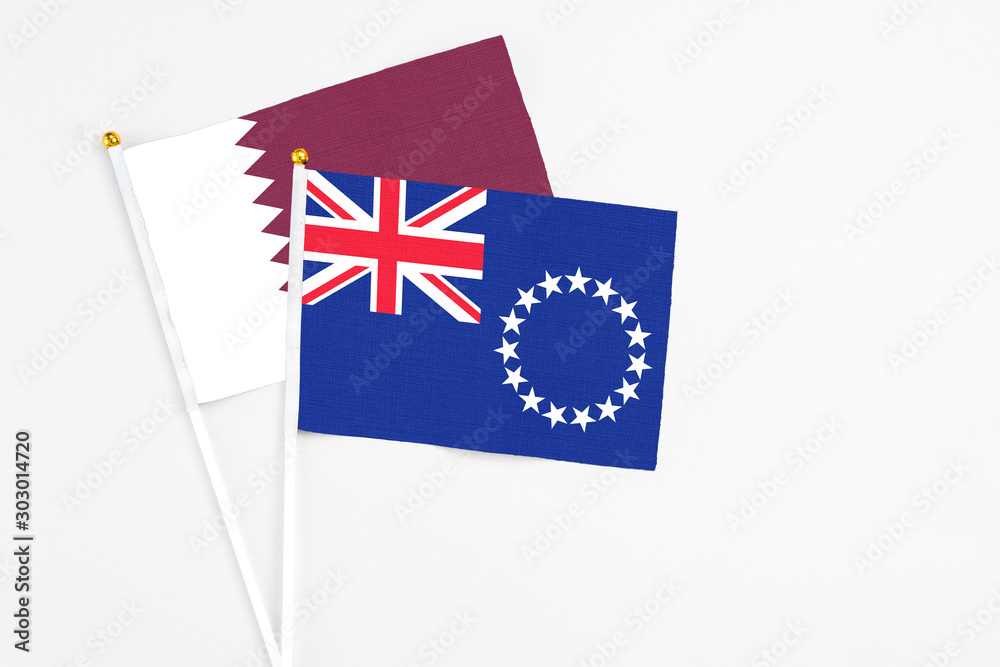 Fototapeta premium Cook Islands and Qatar stick flags on white background. High quality fabric, miniature national flag. Peaceful global concept.White floor for copy space.