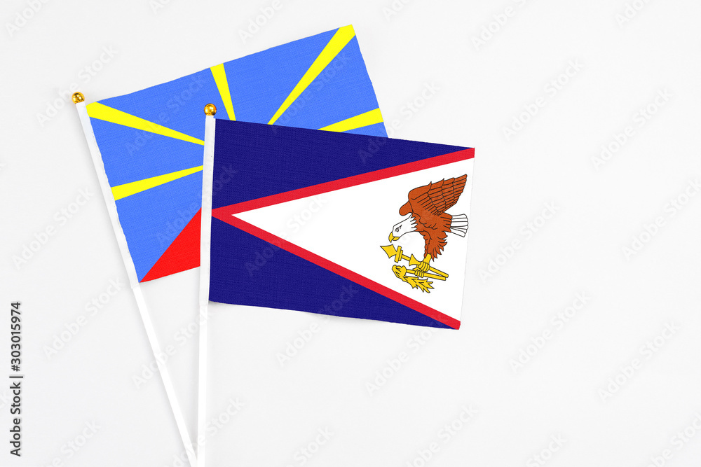 American Samoa and Reunion stick flags on white background. High quality fabric, miniature national flag. Peaceful global concept.White floor for copy space. American Samoa and Reunion stick flags on white background. High quality fabric, miniature national flag. Peaceful global concept.White floor for copy space.