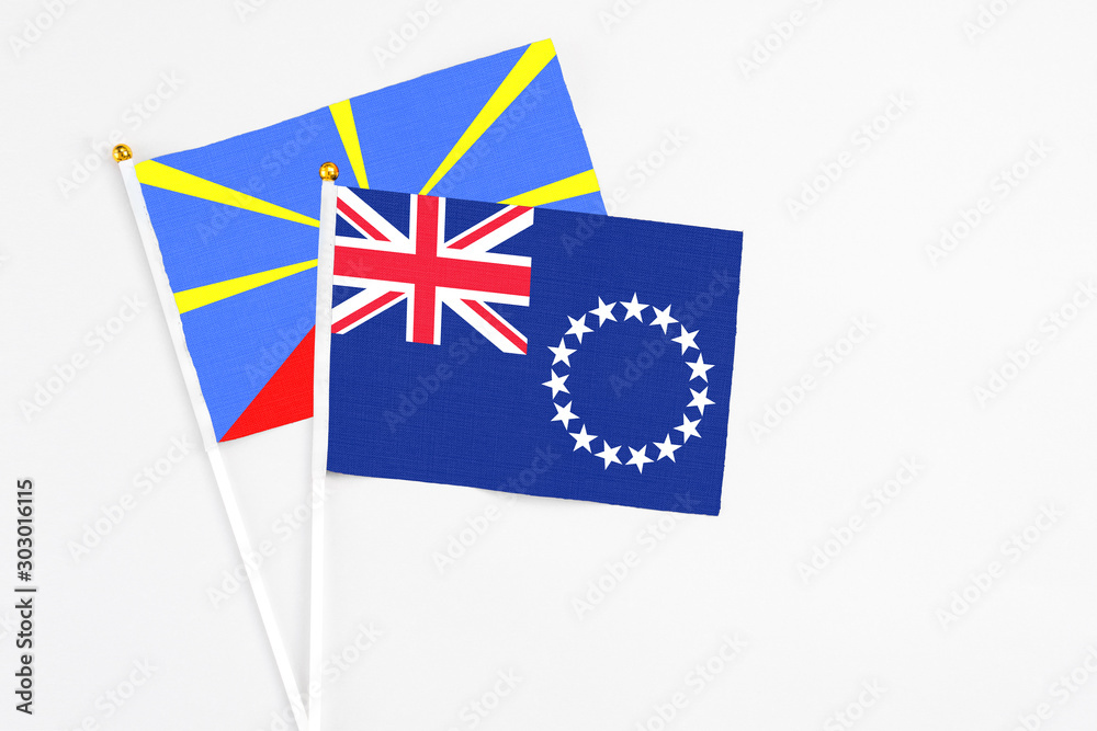 Fototapeta premium Cook Islands and Reunion stick flags on white background. High quality fabric, miniature national flag. Peaceful global concept.White floor for copy space.