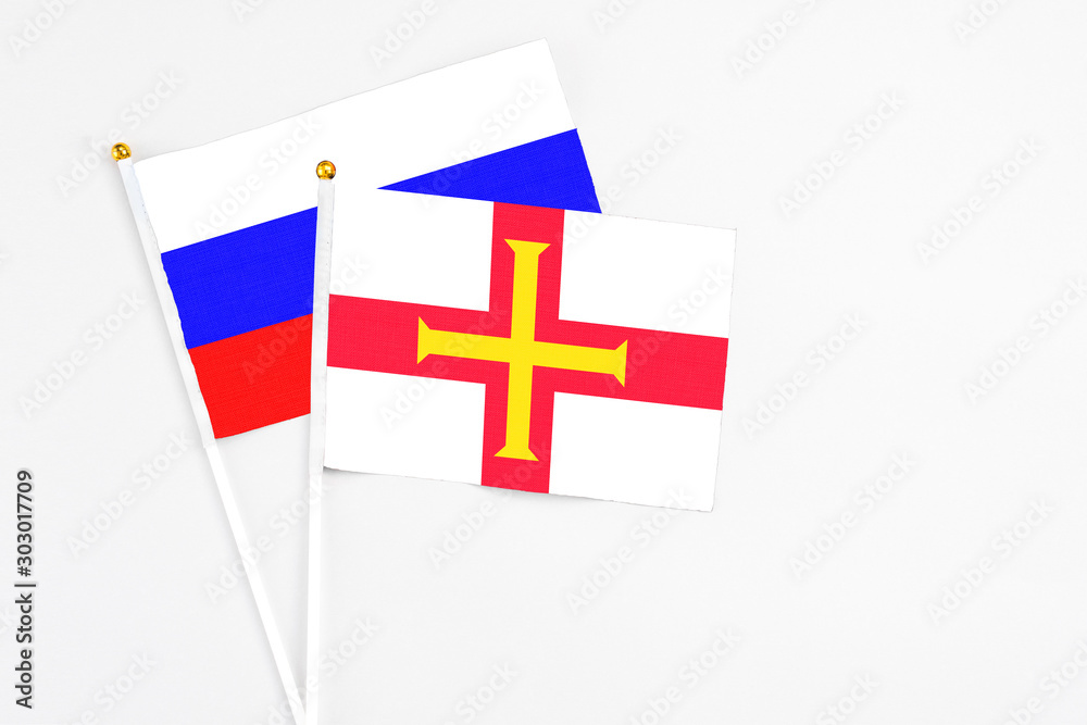 Guernsey and Russia stick flags on white background. High quality fabric, miniature national flag. Peaceful global concept.White floor for copy space.