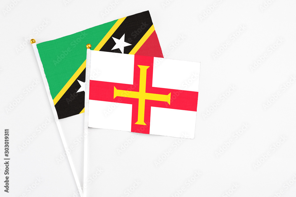 Guernsey and Saint Kitts And Nevis stick flags on white background. High quality fabric, miniature national flag. Peaceful global concept.White floor for copy space.